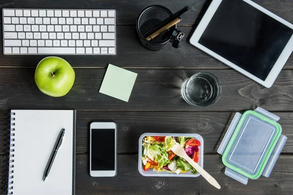 Vue du dessus des appareils numériques avec pomme et salade avec verre d'eau maquette sur table — Photo