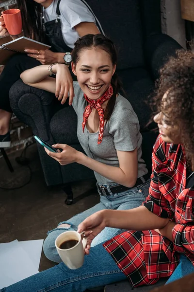 お互いに笑みを浮かべてスマート フォンとコーヒー カップと魅力的な若い女性  — 無料ストックフォト