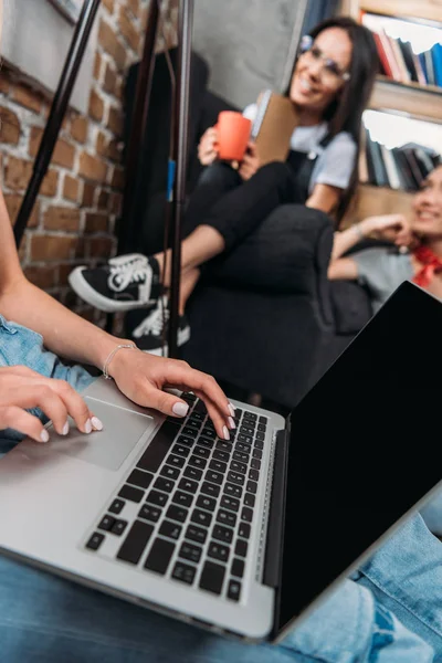 Обрезанный снимок женщины с помощью ноутбука с чистым экраном и улыбающиеся друзья, сидящие позади — стоковое фото