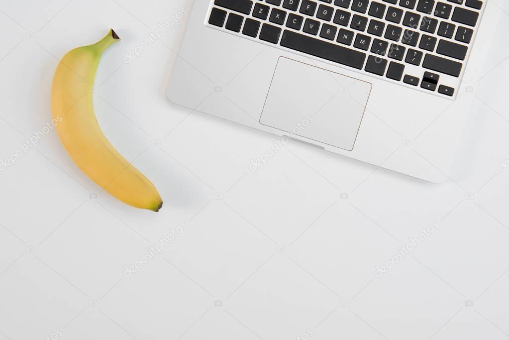 Top view of laptop and fresh ripe banana isolated on grey background