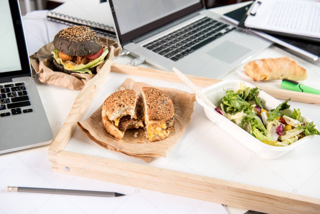 tasty burgers with fresh salad and bread loaf with laptops on tabletop
