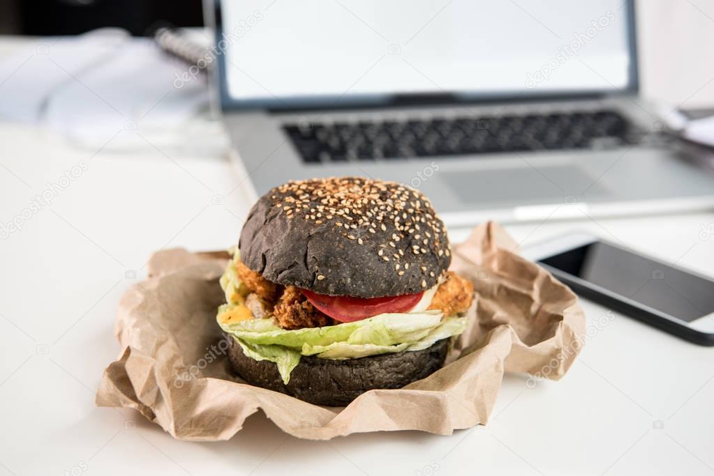 close up of tasty burger with black bun on tabletop at workplace