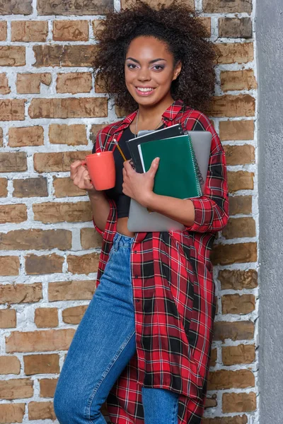 Young stylish african american woman drinking coffee and holding notebook and laptop — Stock Photo