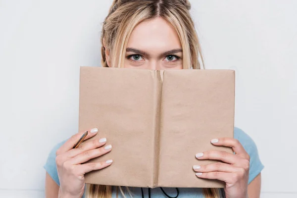 Молодая блондинка держит книгу перед лицом и смотрит в камеру — стоковое фото