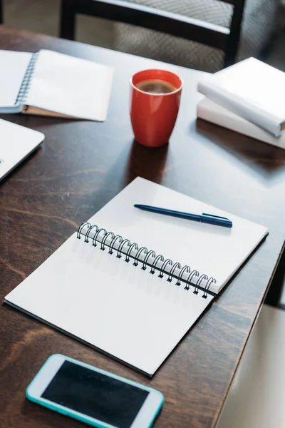 Close up de notebook em branco com caneta e smartphone com xícara de café na mesa — Fotografia de Stock