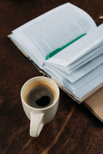 Close up of coffee cup with book and pen on wooden tabletop — Stock Photo