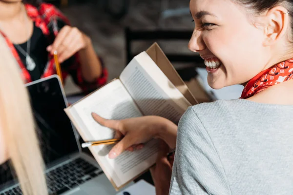 Close up de jovem mulher asiática sorrindo e apontando com o dedo no livro — Fotografia de Stock