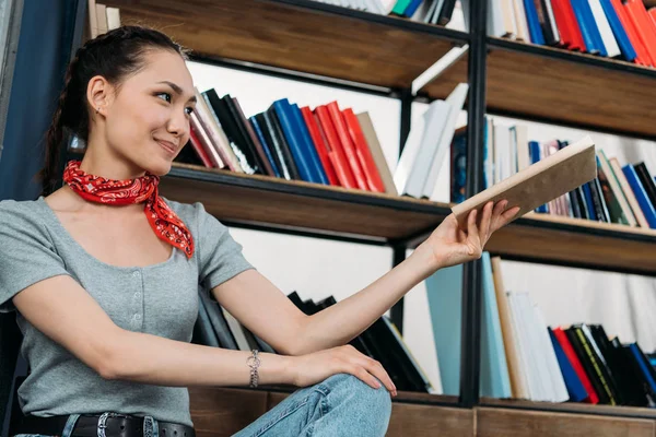 Junge asiatische Frau lächelt und hält Buch zu Hause Bibliothek — Stockfoto