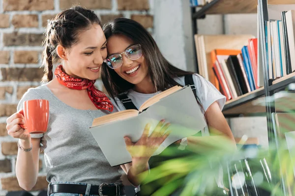 Giovani studenti attraenti con libro e coppa che studiano insieme e sorridono — Foto stock