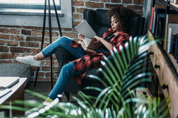 Attractive young african american student sitting on chair with books and digital tablet and studying — Stock Photo