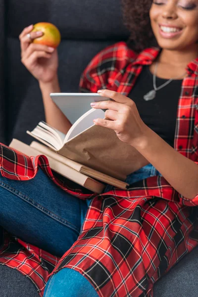 Smiling young woman sitting in chair with books and using digital tablet — Stock Photo