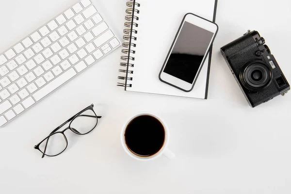 Vista dall'alto di tazza di caffè, tastiera, notebook, occhiali, smartphone e fotocamera sul posto di lavoro — Foto stock