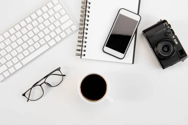 Vue de dessus de tasse de café, clavier, ordinateur portable, lunettes, smartphone et appareil photo sur le lieu de travail — Photo de stock