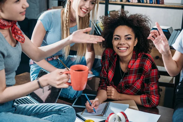 Gruppo multietnico di giovani donne sorridenti che bevono caffè e studiano insieme — Foto stock