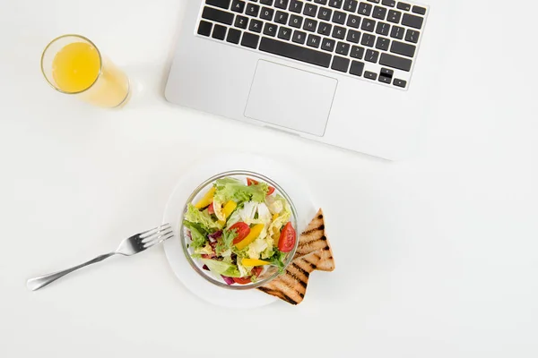 Vista superior de la computadora portátil, jugo de naranja en vidrio y ensalada sana fresca con tostadas en el lugar de trabajo — Stock Photo