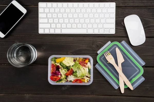 Vue du dessus du smartphone, du clavier d'ordinateur et de la souris d'ordinateur avec salade fraîche sur table en bois . — Photo de stock