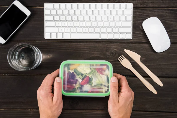 Вид зверху на робоче місце з цифровими пристроями і людськими руками, здатними їсти салат під час роботи — стокове фото