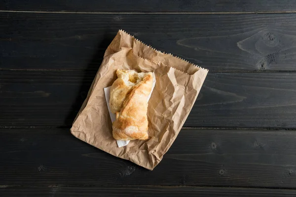 Vista superior de bollo de pastelería mordida en bolsa de papel en mesa de madera - foto de stock