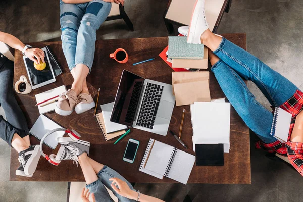 Imagen recortada de los estudiantes sentados en la mesa con libros y dispositivos digitales - foto de stock