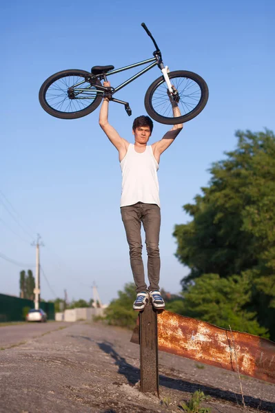 De jongen met de zilveren fiets overhead staande op een ijzeren paal — Stockfoto