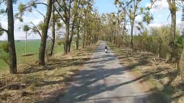 Una chica monta un ciclomotor en un callejón con árboles — Vídeos de Stock