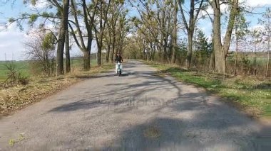 Bir kız bir ara sokakta ağaçları ile üzerinde bir motosiklet sürme