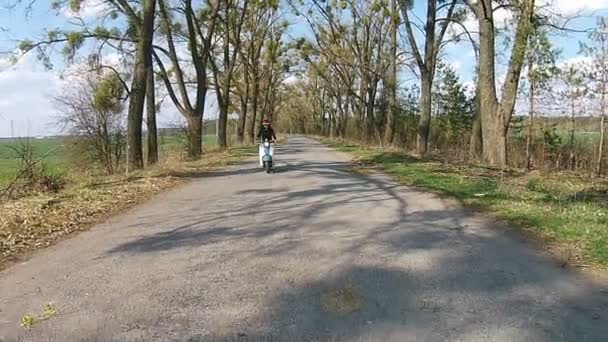 Une fille roule sur un cyclomoteur dans une ruelle avec des arbres — Video