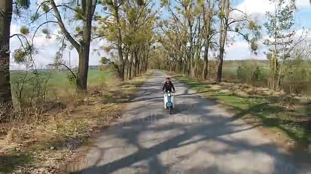 Ein Mädchen fährt mit einem Moped auf einer Allee mit Bäumen — Stockvideo