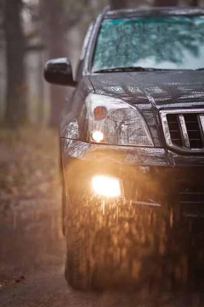 Nahaufnahme Vorderseite des schwarzen Geländewagens im Wald bei Regen — Stockfoto
