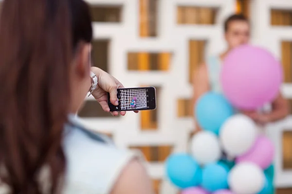 Menina tira fotos de um cara em um telefone com balões — Fotografia de Stock