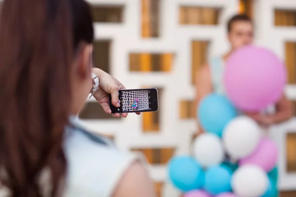 Dívka bere obrázky chlapa na telefonu s balónky — Stock fotografie