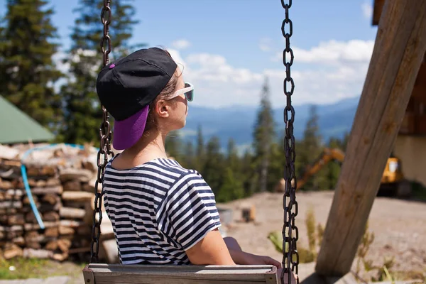 En ung flicka som rider på en gunga med utsikt över bergen — Stockfoto