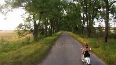 Bir kız bir ara sokakta ağaçları ile üzerinde bir motosiklet sürme