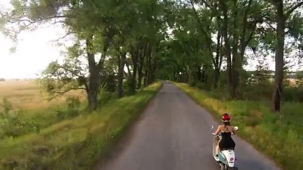 Une fille roule sur un cyclomoteur dans une ruelle avec des arbres — Video