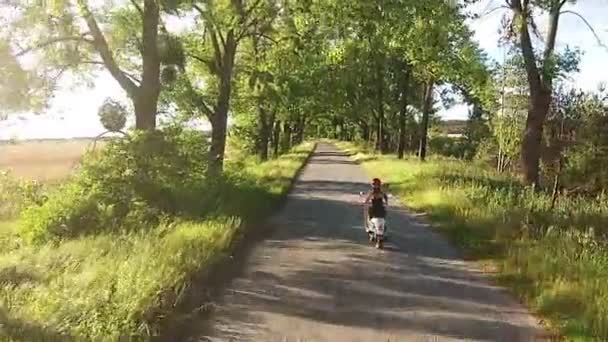 En tjej rider en moped på en gränd med träd — Stockvideo