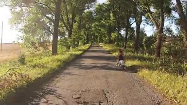 En tjej rider en moped på en gränd med träd — Stockvideo