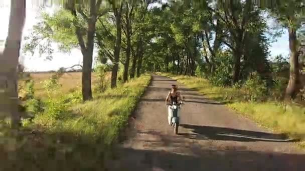 一个女孩正骑一辆摩托车在巷子，树上 — 图库视频影像