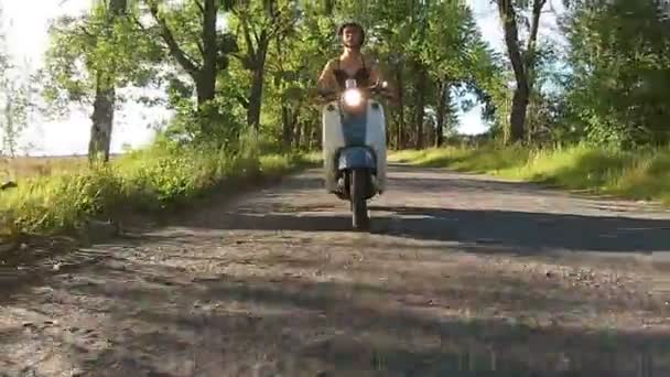 Een meisje is een bromfiets rijden op een steegje met bomen — Stockvideo