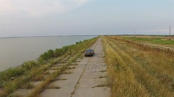 Aparat, dron śledzi samochodu, który jedzie wzdłuż nasypu w pobliżu morza — Wideo stockowe