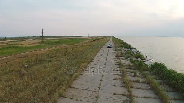 La cámara en el dron rastrea el coche, que cabalga a lo largo del terraplén cerca del mar — Vídeos de Stock