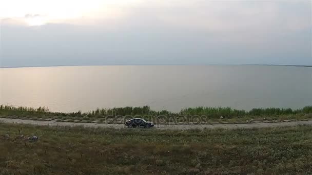 Камера на беспилотнике отслеживает автомобиль, который едет вдоль насыпи у моря — стоковое видео