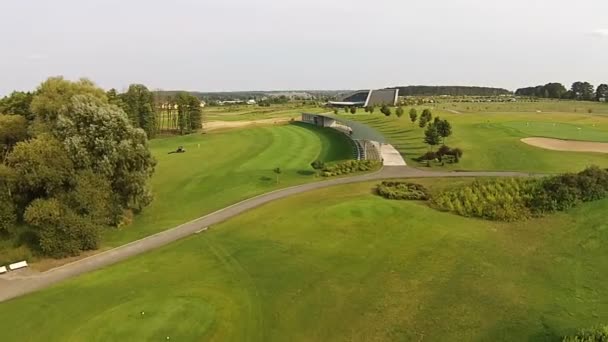 Беспилотник пролетает над зеленым полем для гольфа со строительством — стоковое видео