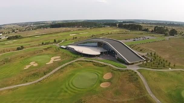 Беспилотник пролетает над зеленым полем для гольфа со зданием гольф-клуба — стоковое видео