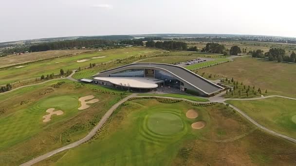 En drönare flyger över en grön golfbana med golfklubb byggnad — Stockvideo