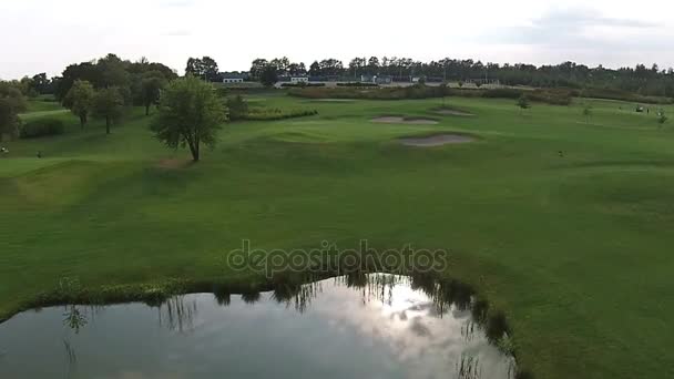 Беспилотник летит над зеленым полем для гольфа с озером — стоковое видео