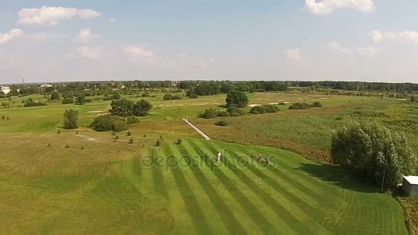 En drönare flyger över en grön golfbana med mans spela golf — Stockvideo