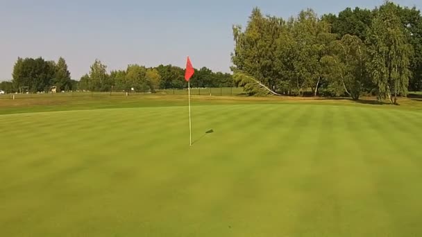 Een drone vliegt over goed met vlag boven de groene golfbaan — Stockvideo