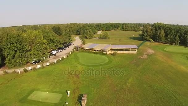 En drönare flyger över en grön golfbana med golfklubb byggnad — Stockvideo