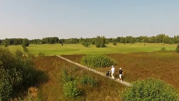 Дрон летить над зеленим полем для гольфу, де люди ходять — стокове відео