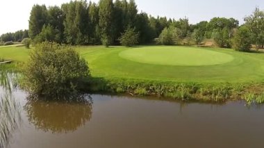 Göl ile yeşil bir golf sahası üzerinde bir uçak uçar